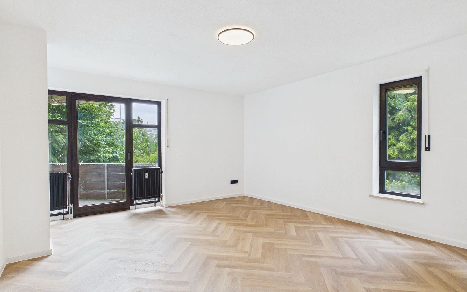 Leeres, saniertes Wohnzimmer mit Fischgrätparkett und hohen Fenstern