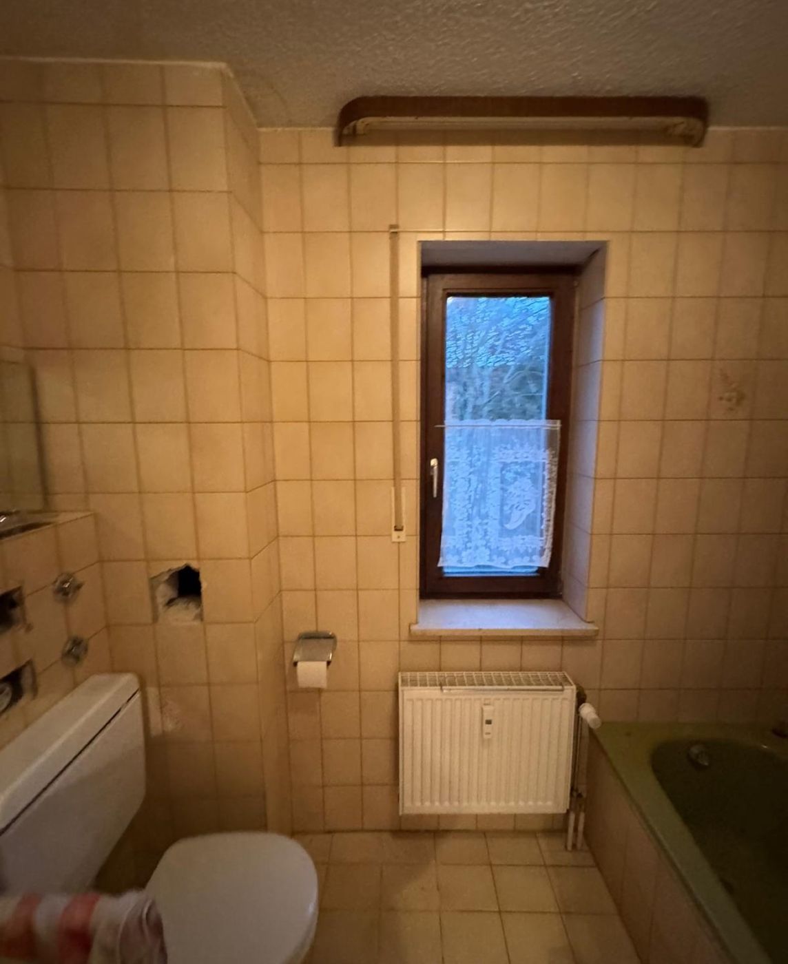 Badezimmer vor der Sanierung mit alten Fliesen, Badewanne und Fenster